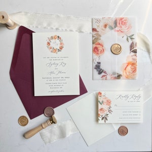 May include: A wedding invitation suite with a floral design. The invitation features a wreath of flowers in shades of orange, pink, and green. The RSVP card features a similar floral design with a pink and white color scheme. The text on the invitation reads "You are invited to celebrate the marriage of..." and the text on the RSVP card reads "Kindly Reply by July 5, 2023".