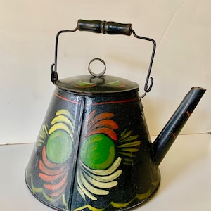 Könnte beinhalten: Schwarze Metallkanne mit einem bemalten Blumendesign in Gelb, Orange und Grün. Die Kanne hat einen schwarzen Holzgriff und einen Ausguss. Der Deckel hat einen kleinen Ringgriff. Es ist ein Vintage- oder antiker Artikel.