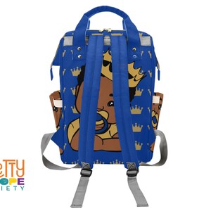 Puede incluir: Mochila azul con un beb&eacute; de dibujos animados con corona y chupete. La mochila tiene un patr&oacute;n repetido de coronas doradas sobre un fondo azul. Tiene correas azules, correas grises para los hombros y bolsillos laterales.