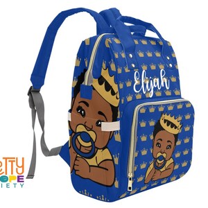 Puede incluir: Mochila azul para beb&eacute; con un estampado de coronas doradas y un beb&eacute; de dibujos animados con corona y chupete. El nombre "Elijah" est&aacute; escrito en blanco. La mochila tiene correas ajustables y m&uacute;ltiples compartimentos.