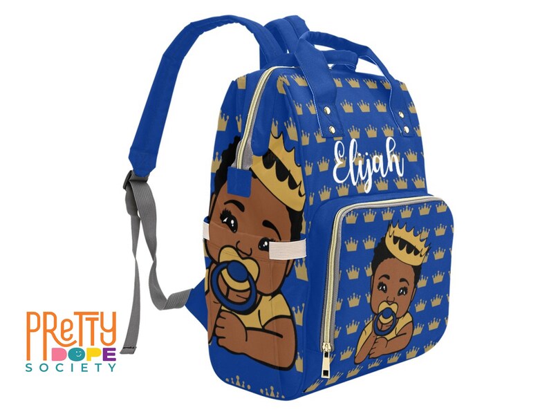Puede incluir: Mochila azul para beb&eacute; con un estampado de coronas doradas y un beb&eacute; de dibujos animados con corona y chupete. El nombre "Elijah" est&aacute; escrito en blanco. La mochila tiene correas ajustables y m&uacute;ltiples compartimentos.