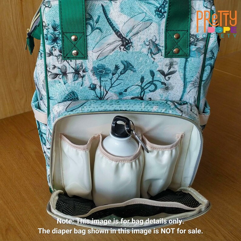 Puede incluir: Un bolso de pa&ntilde;ales turquesa y blanco con un estampado de lib&eacute;lulas y flores. El bolso tiene correas verdes y un bolsillo frontal con una botella de agua blanca. El bolso tiene m&uacute;ltiples bolsillos para guardar cosas. El texto en el bolso dice "PRETTY SOCIETY".