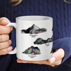 May include: White ceramic mug featuring a watercolour illustration of three mountains. The mountains are labelled "Schiehallion 1083m", "Carn Gorm 1238m", and "Ben Narnain 926m".