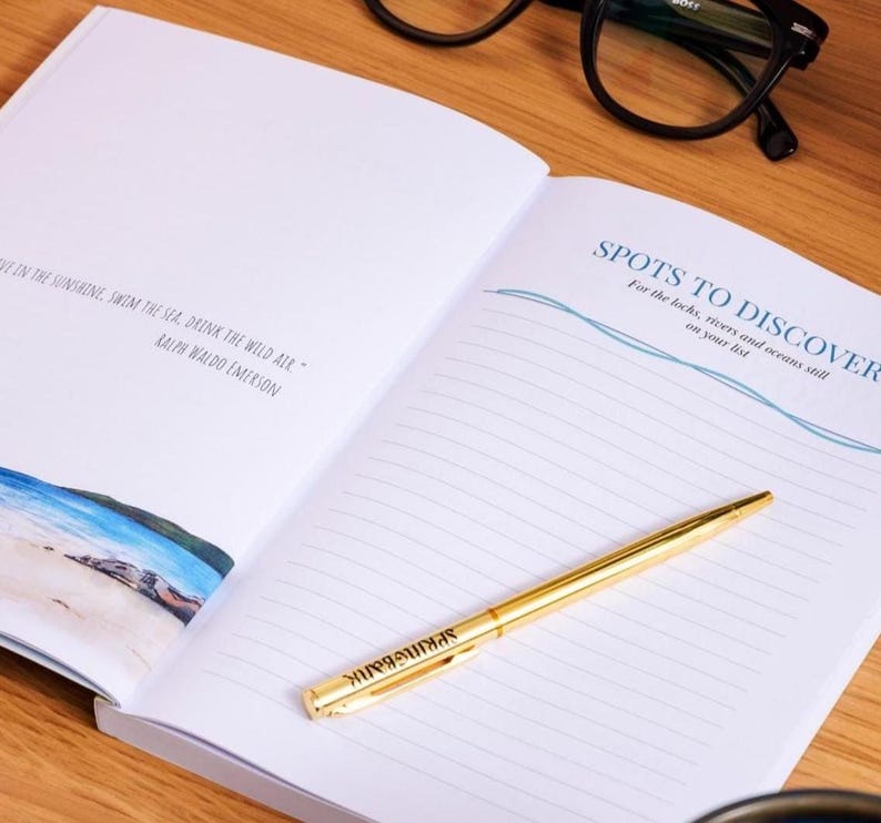 May include: An open notebook with lined pages and the text "SPOTS TO DISCOVER" in blue. A gold pen rests on the page. The notebook also features a quote by Ralph Waldo Emerson. Black glasses are in the background.