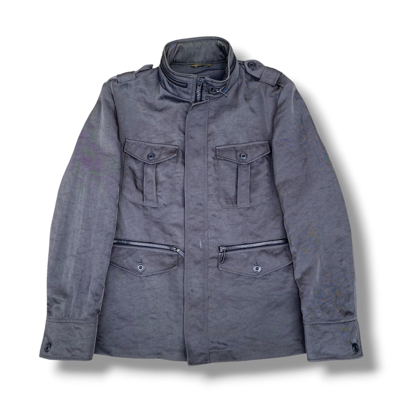 K&ouml;nnte beinhalten: Eine dunkelgraue Utility-Jacke mit hohem Kragen und Rei&szlig;verschluss-Detail, Schulterklappen und langen &Auml;rmeln mit gekn&ouml;pften Manschetten. Die Vorderseite hat zwei Brusttaschen mit Knopfklappen und zwei untere Rei&szlig;verschlusstaschen mit Knopfklappen.