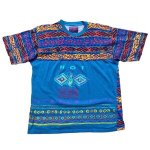 Puede incluir: Una camiseta azul de manga corta con un estampado geométrico colorido en la parte superior e inferior. La camiseta tiene las palabras "HOT" y "CHILL" impresas en la parte delantera en una fuente colorida y estilizada.