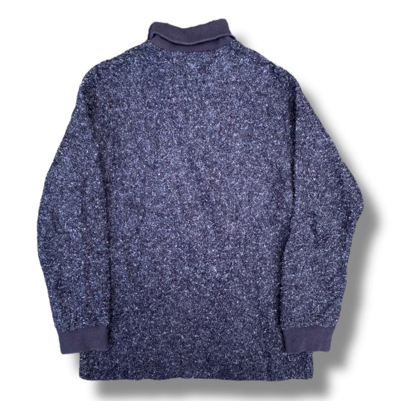 K&ouml;nnte beinhalten: Ein marineblauer Langarmpullover mit einem strukturierten, gesprenkelten Muster. Der Pullover hat einen dunkelblauen Kragen und Manschetten. Der Stoff scheint ein dickes Strickgewebe zu sein, das f&uuml;r k&uuml;hleres Wetter geeignet ist.