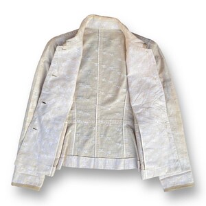May include: A white linen jacket with a button closure and long sleeves. The jacket is unbuttoned and the lining is visible. The lining has a white pattern.