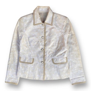 May include: A beige blazer with a white patterned design and a brown trim. The blazer has a button-up front and long sleeves.