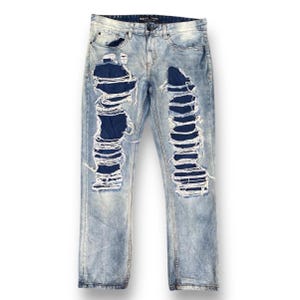 Peut inclure: Jean en denim bleu clair délavé à l'acide avec de larges panneaux déchirés et effilochés sur le devant des deux jambes, révélant un tissu en denim bleu foncé en dessous. Le jean comprend une braguette à boutons, des passants et cinq poches.