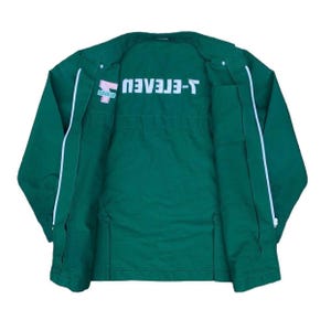 May include: A dark green jacket with white trim and the text "T-ELEVEN" in white. The jacket has a zipper closure and two front pockets. The logo is on the left chest.