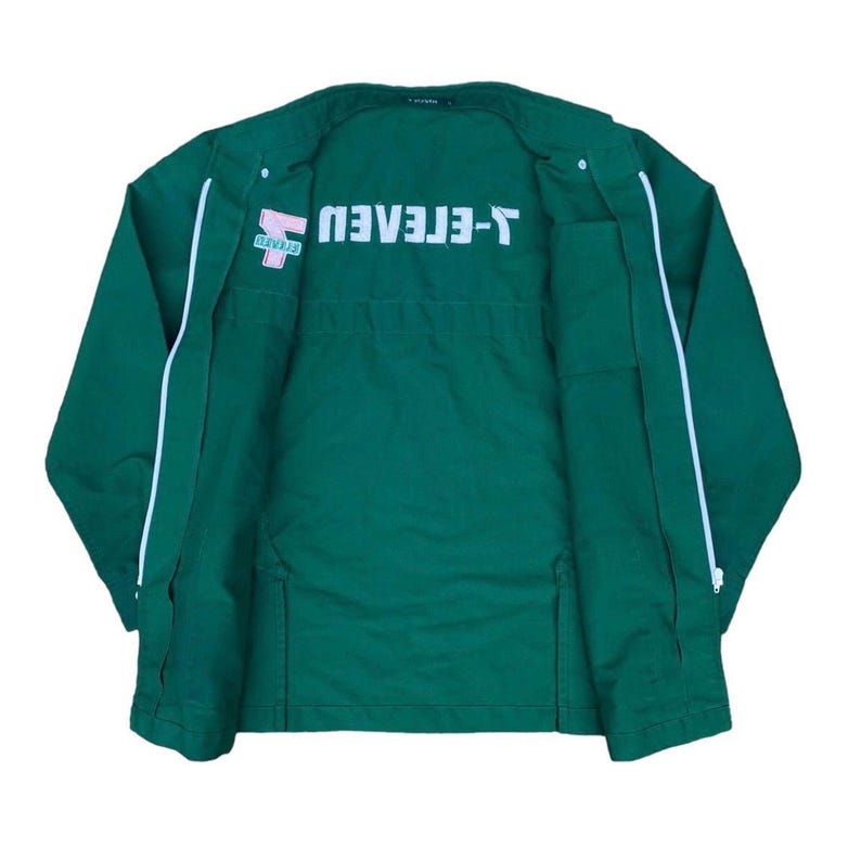 May include: A dark green jacket with white trim and the text "T-ELEVEN" in white. The jacket has a zipper closure and two front pockets. The logo is on the left chest.