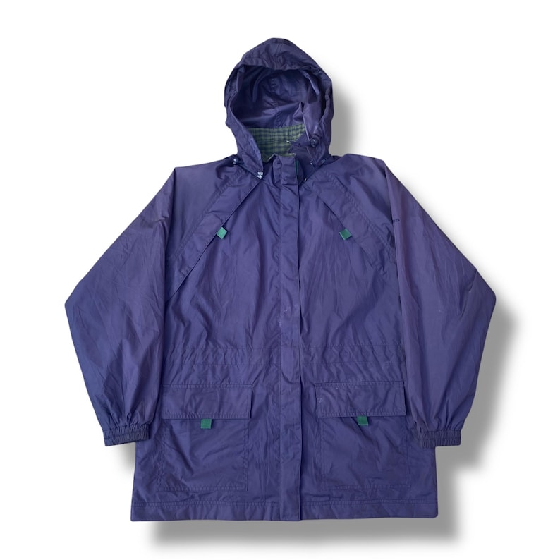 May include: A purple hooded rain jacket with a green and gray plaid lining visible in the hood. The jacket has two front pockets and green accents. The sleeves have elastic cuffs. The jacket is designed for outdoor wear.