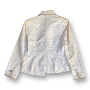 May include: A white blazer with a subtle pattern. The blazer has a collar, long sleeves, and a button closure. The blazer is made of a lightweight fabric.