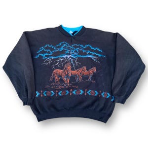 Könnte beinhalten: Schwarzer Pullover mit einem Aufdruck von drei braunen Pferden, die durch einen stürmischen Himmel mit Blitzen rennen. Der Aufdruck ist von einem blauen und braunen geometrischen Muster umgeben.
