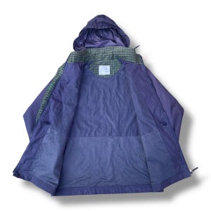 May include: A purple and green hooded jacket, open to display the interior lining. The jacket features a plaid pattern on the shoulders and hood, with a solid purple body. The jacket has a zipper closure and a small logo patch.