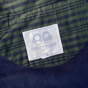 May include: Close-up of a navy blue garment with a green and navy plaid lining. A white label with the text "AC sport futur courr&egrave;ges paris" is sewn into the garment.