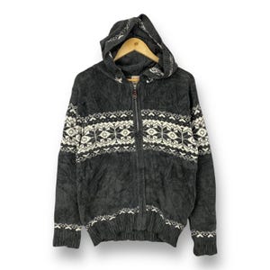 Puede incluir: Una sudadera gris con capucha y un patrón de copo de nieve blanco. La sudadera tiene una cremallera y un ajuste holgado.