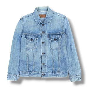 Könnte beinhalten: Hellblaue Jeansjacke mit klassischem Kragen, Knopfleiste und zwei Brusttaschen. Die Jacke hat eine verwaschene Optik und ein kleines rotes Etikett auf der Tasche. Ein zeitloses Oberbekleidungsstück.