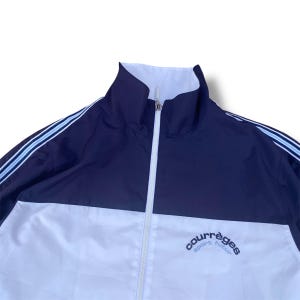 May include: A navy blue and white track jacket with a high collar and a full-length zipper. The jacket features white stripes on the sleeves and the brand name "courr&egrave;ges sport futur" in cursive on the chest.