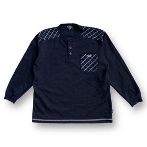 Puede incluir: Camiseta negra de manga larga con un patrón de diamantes en los hombros y un bolsillo. La camisa tiene un cuello abotonado y el nombre de la marca "Sacony" está impreso en el cuello y el bolsillo.