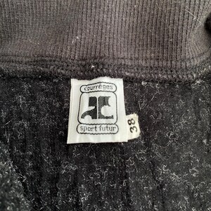 K&ouml;nnte beinhalten: Nahaufnahme eines schwarzen Kleidungsst&uuml;cks mit gerippter Struktur. Ein wei&szlig;es Etikett zeigt den Markennamen "courr&egrave;ges" &uuml;ber einem Logo und die Worte "sport futur". Die Nummer "38" ist auf einem separaten Etikett aufgedruckt.