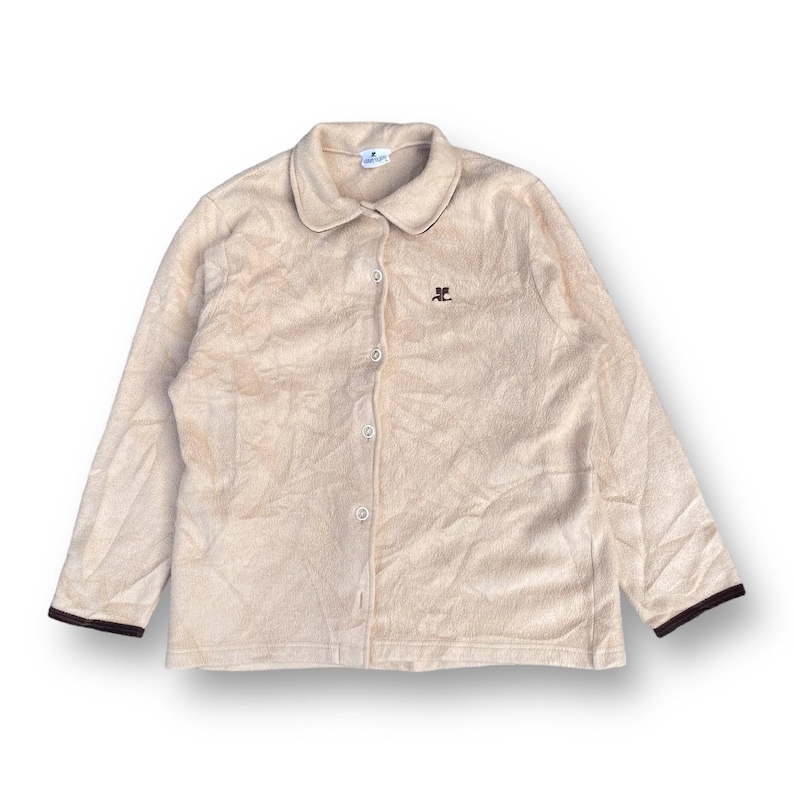 May include: A beige button-up shirt with long sleeves and a brown embroidered logo on the left chest. The shirt has a collar and a button-up front.