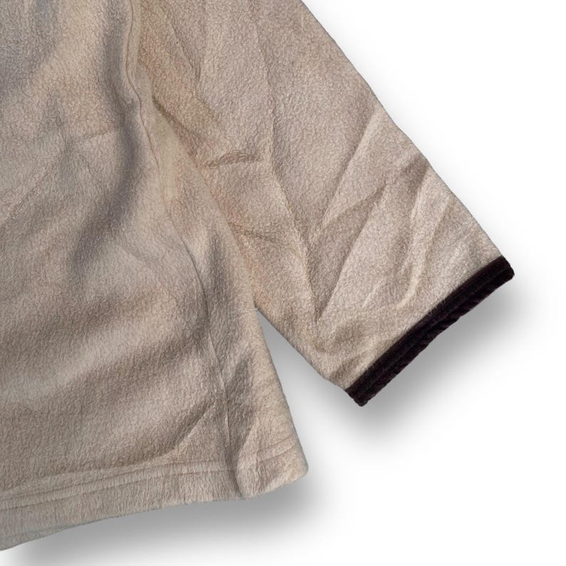 May include: A cream-colored fleece jacket with a brown trim around the edges. The jacket has a textured surface and a relaxed fit.