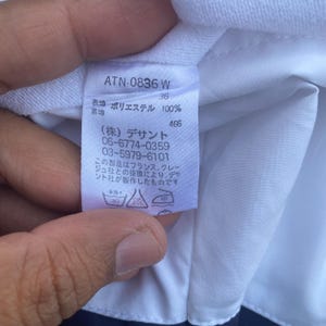 May include: A close-up of a white clothing tag with Japanese text and the number "36". The tag also includes the text "ATN-0836 W" and "ポリエステル 100%" and care symbols.