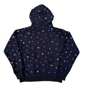 Puede incluir: Sudadera con capucha negra con un estampado de estrellas de colores. Las estrellas son en tonos rosa, amarillo, azul y morado. La sudadera tiene una capucha con cord&oacute;n y pu&ntilde;os y dobladillo de canal&eacute;.