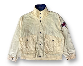 May include: A yellow jacket with a blue and red logo patch on the right sleeve. The jacket has a high collar, a button-up front, and two large pockets on the front.