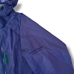 May include: A close-up of a navy blue jacket with a hood. The jacket has a zipper closure and a green velcro patch. The words "courr&egrave;ges sport futur" are printed on the sleeve.