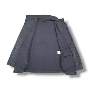 K&ouml;nnte beinhalten: Eine anthrazitfarbene Rei&szlig;verschlussjacke von innen betrachtet, mit Stehkragen, langen &Auml;rmeln und zwei Innentaschen. Ein kleines schwarzes Etikett mit dem wei&szlig;en Text A.A.R ist an der unteren rechten Innentasche zu sehen.