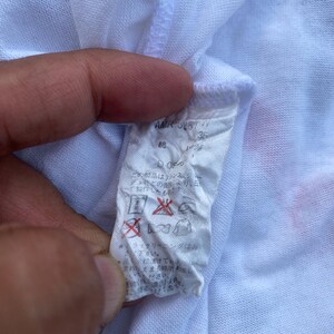 K&ouml;nnte beinhalten: Wei&szlig;es Kleidungsetikett mit japanischem Text und Symbolen. Das Etikett enth&auml;lt den Text "AMR 5157" und "35".