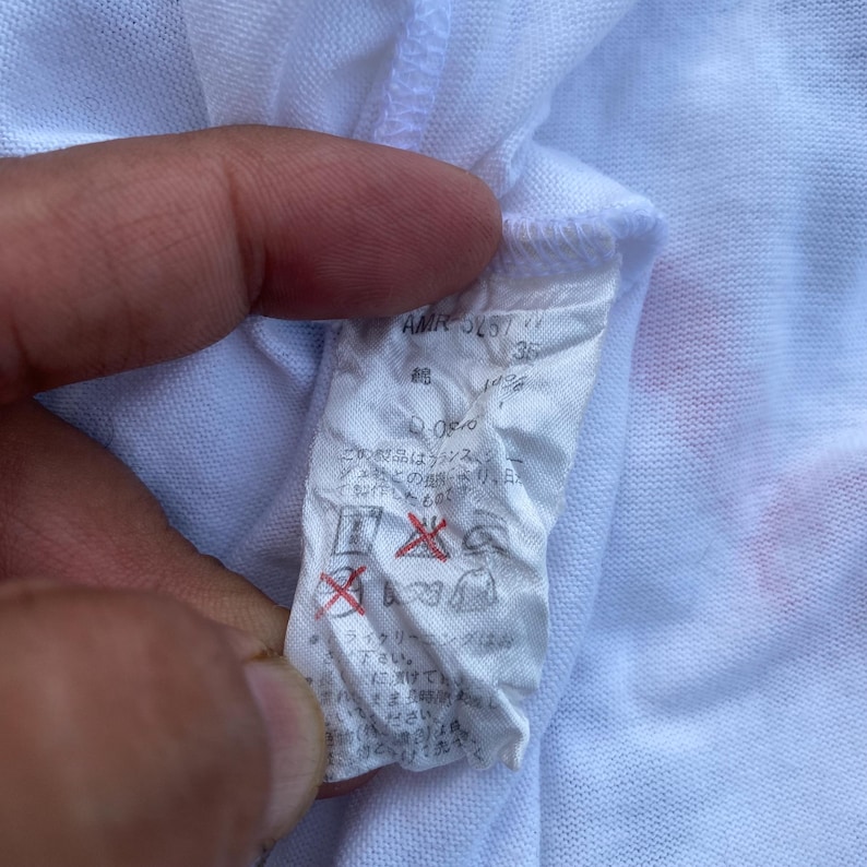 K&ouml;nnte beinhalten: Wei&szlig;es Kleidungsetikett mit japanischem Text und Symbolen. Das Etikett enth&auml;lt den Text "AMR 5157" und "35".