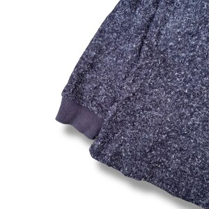 K&ouml;nnte beinhalten: Nahaufnahme eines dunkelblauen Sweatshirt-&Auml;rmels mit einem strukturierten, gesprenkelten Muster. Das B&uuml;ndchen ist einfarbig, dunkleres Blau. Der Stoff wirkt weich und bequem, geeignet f&uuml;r Freizeitkleidung.