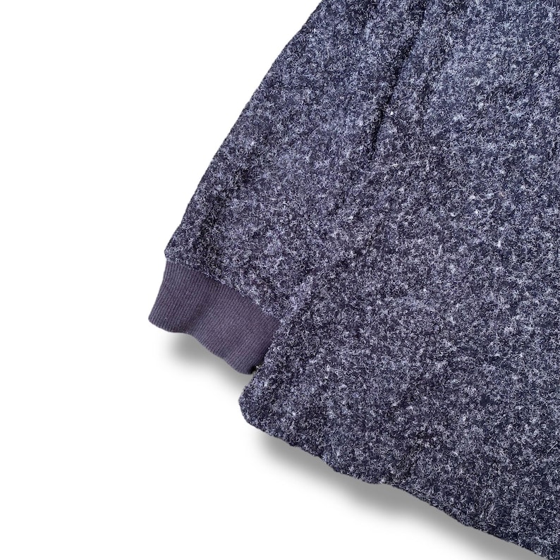 K&ouml;nnte beinhalten: Nahaufnahme eines dunkelblauen Sweatshirt-&Auml;rmels mit einem strukturierten, gesprenkelten Muster. Das B&uuml;ndchen ist einfarbig, dunkleres Blau. Der Stoff wirkt weich und bequem, geeignet f&uuml;r Freizeitkleidung.
