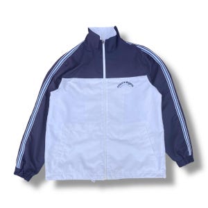 May include: A navy and white track jacket with a full zipper and a high collar. The jacket has two light blue stripes down each sleeve and the word "courr&egrave;ges" is printed on the chest.