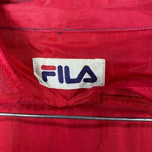Op de afbeelding: Rood jack met een wit Fila-logo op de voorkant. Het logo is in blauwe en rode letters.