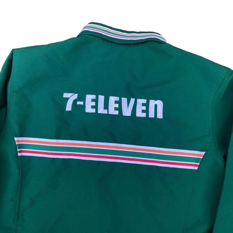 May include: A green jacket with the text "7-ELEVEN" in white block letters across the back. The jacket has a striped design in red, white, and orange near the bottom. The collar has a striped design in white, green, and red.