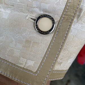 May include: Close-up of a white fabric with a beige leather trim and a silver button with the text "COUGAR" embossed on it.