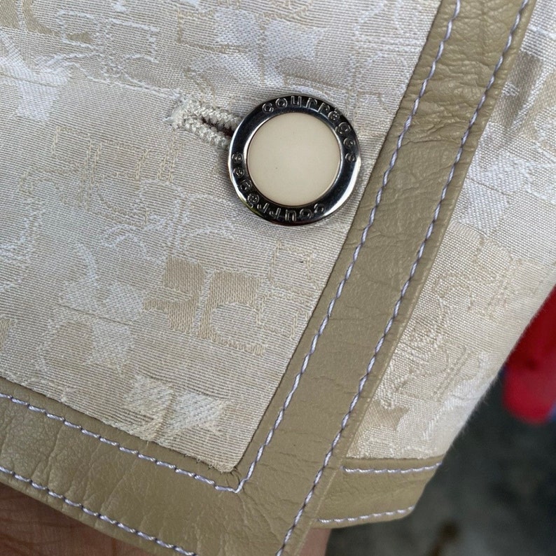 May include: Close-up of a white fabric with a beige leather trim and a silver button with the text "COUGAR" embossed on it.