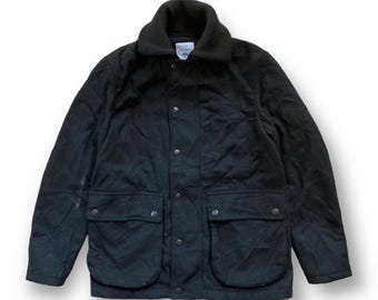 Può includere: Giacca trapuntata nera con colletto a coste e quattro tasche frontali. La giacca ha una chiusura con bottoni e un design classico. La giacca è di colore scuro e sembra essere realizzata in un materiale resistente.