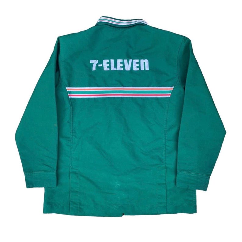 May include: Green long-sleeved work shirt with the text "7-ELEVEN" across the back. The shirt has a striped design in red, white, and green across the back. The collar has a striped design in white, green, and blue.