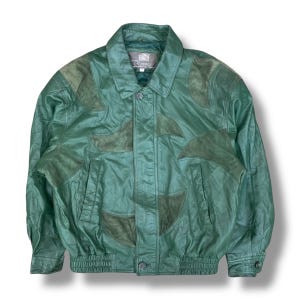 Op de afbeelding: Groene leren jas met suède details. De jas heeft een kraag, knoopsluiting en twee voorzakken. Het heeft een bomberstijl met geribde manchetten en zoom. Het label luidt "Rommy".