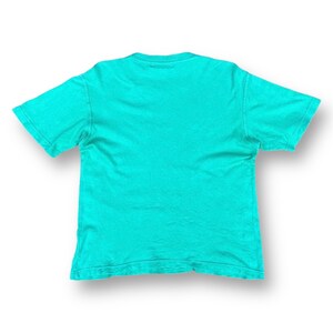 Puede incluir: Una camiseta lisa de color azul turquesa con mangas cortas.