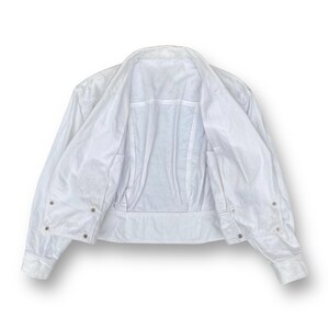 May include: A white cropped jacket with long sleeves and a button-up front. The jacket is unbuttoned and turned inside out, showing the lining.