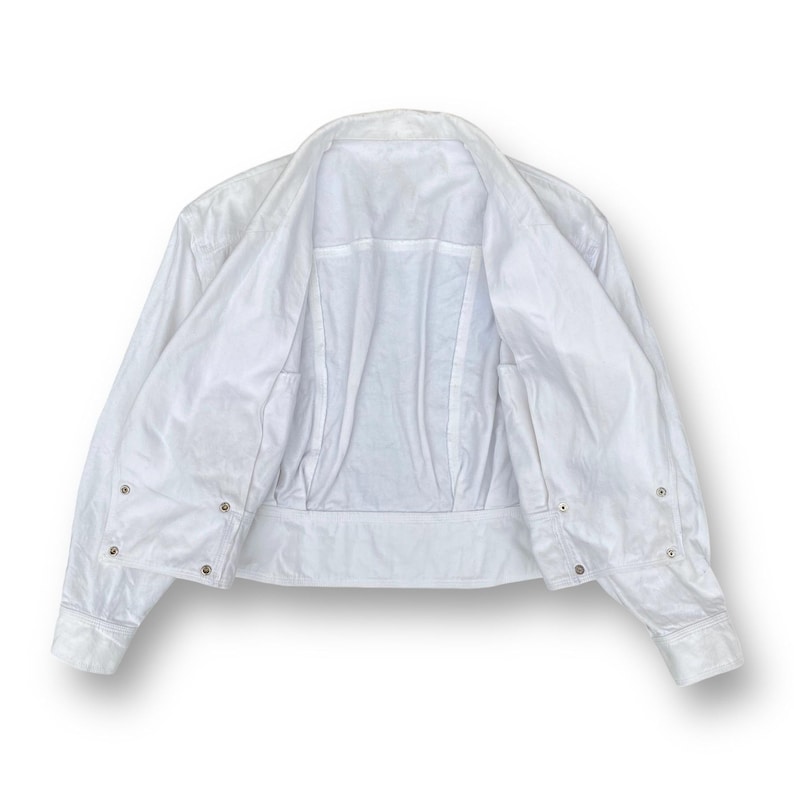 May include: A white cropped jacket with long sleeves and a button-up front. The jacket is unbuttoned and turned inside out, showing the lining.