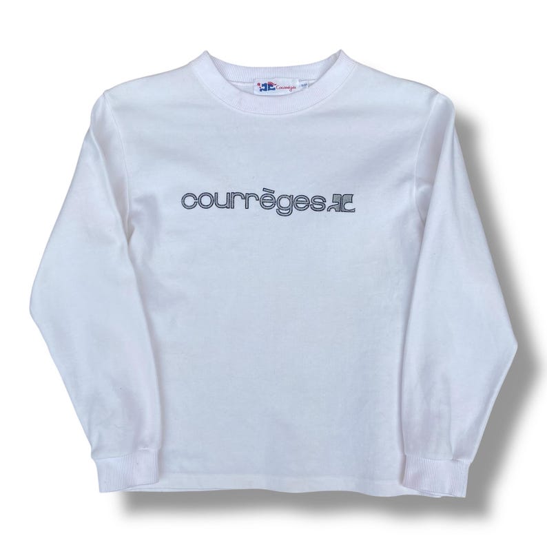 May include: White long-sleeve shirt with the text "courr&egrave;ges.ac" in a dark blue font across the chest. The shirt has a crew neck and ribbed cuffs. The brand logo is visible on the upper back of the shirt.