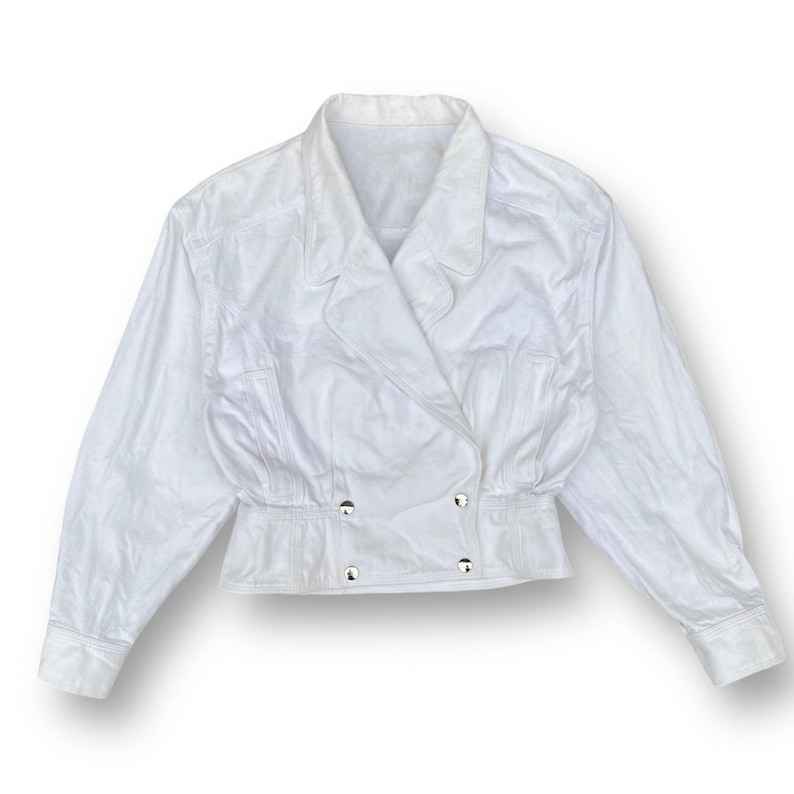 May include: A white cropped jacket with a double-breasted closure and long sleeves.